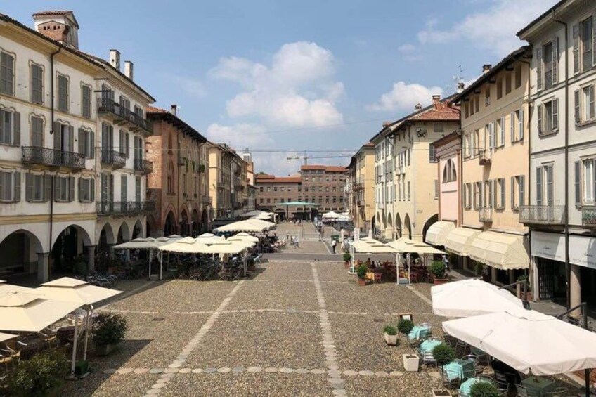 A cobblestone square with buildings on either side, outdoor seating areas, and a clear sky. 5