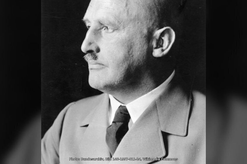 A person wearing a light-colored suit with a dark tie and a lapel pin. 3
