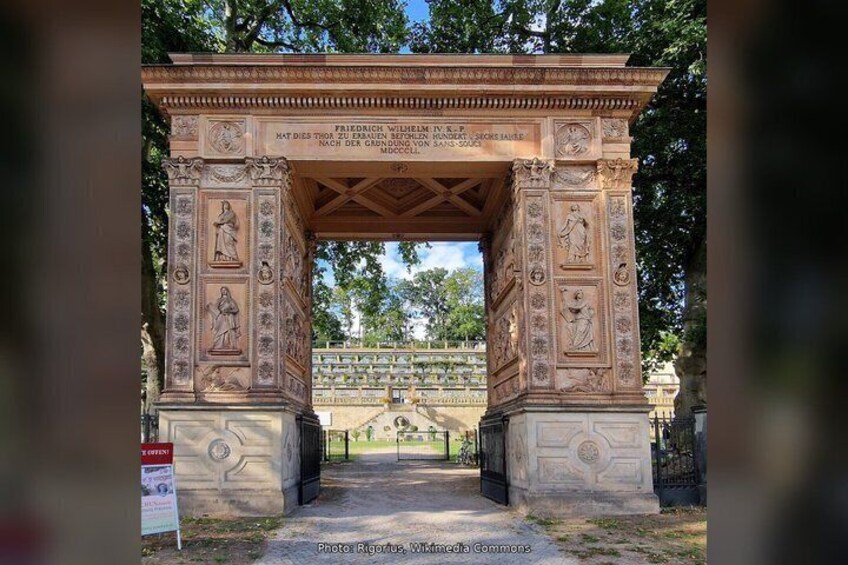 An ornate stone archway with intricate carvings and inscriptions, surrounded by trees. 5