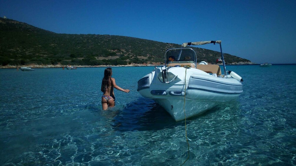 A woman in a bikini standing in shallow water next to a boat. 1