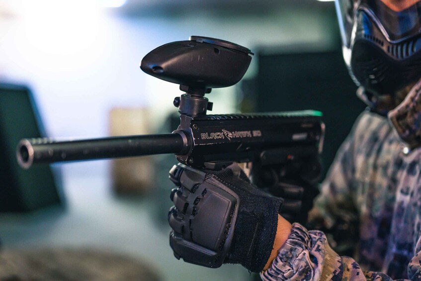A person holding a paintball gun with a scope, wearing a mask and gloves. 5
