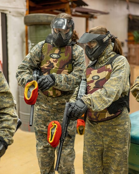 Two people in paintball gear holding paintball guns and masks. 3