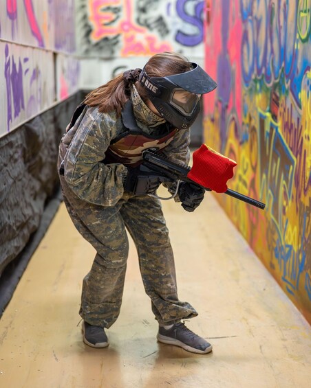 A person in camouflage paintball gear crouching in an alley with colorful graffiti on the walls. 1