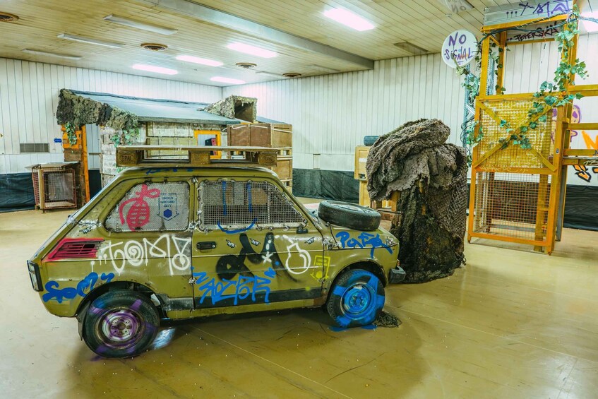 A graffiti-covered car with a makeshift roof and tires on the back, parked indoors with wooden walls and graffiti on the ceiling. 5