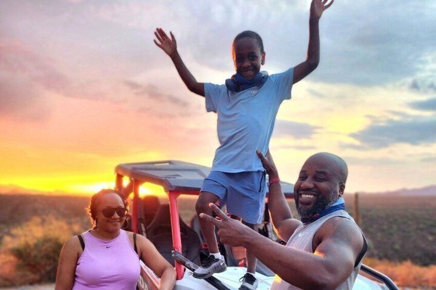 Three people on a vehicle with a sunset in the background. 3