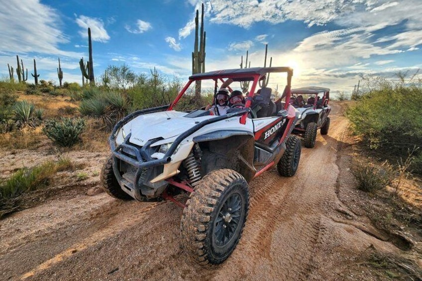 A white and red off-road vehicle on a dirt path with cacti and desert vegetation in the background. 4