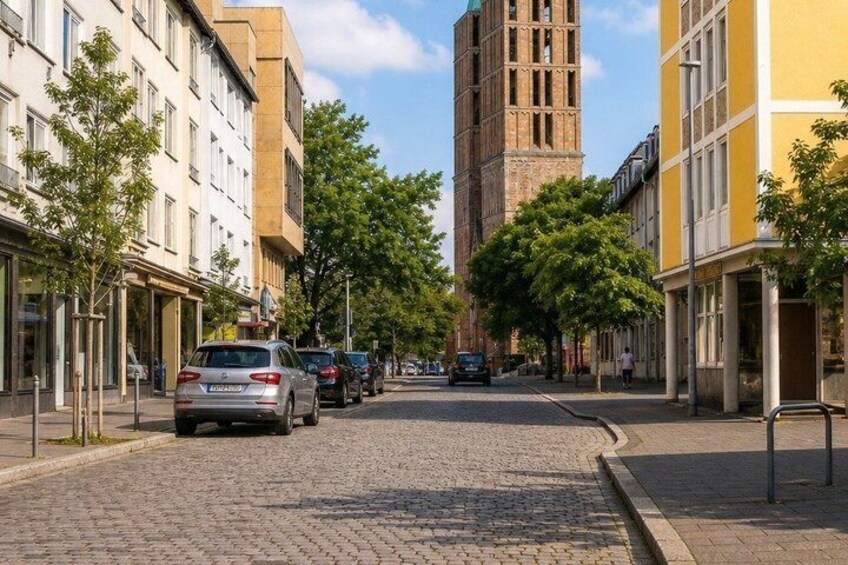 A cobblestone street lined with trees and buildings, including a prominent tower. 3