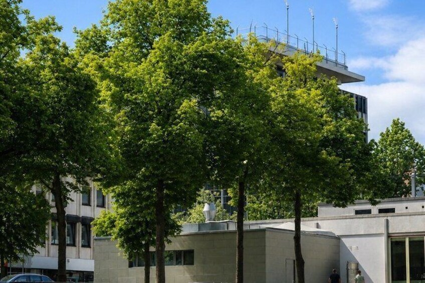 A modern building with a flat roof, surrounded by lush green trees. 2