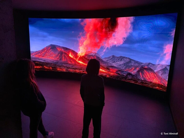 A large digital display of a volcanic landscape with lava flows and a person standing in front of it. 4