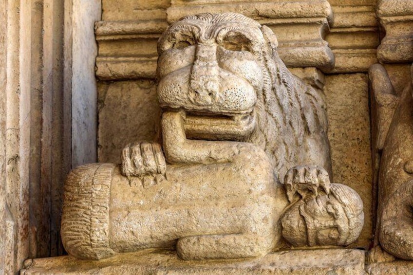 A stone lion sculpture with a detailed mane and paws, set against a stone wall. 2