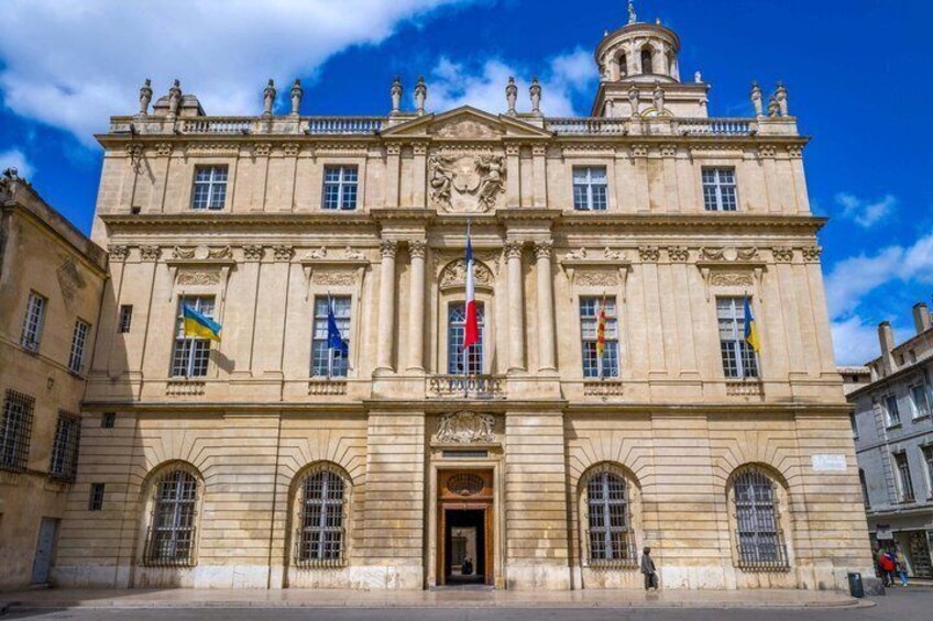A historic building with a central entrance, arched windows, and flags. 3
