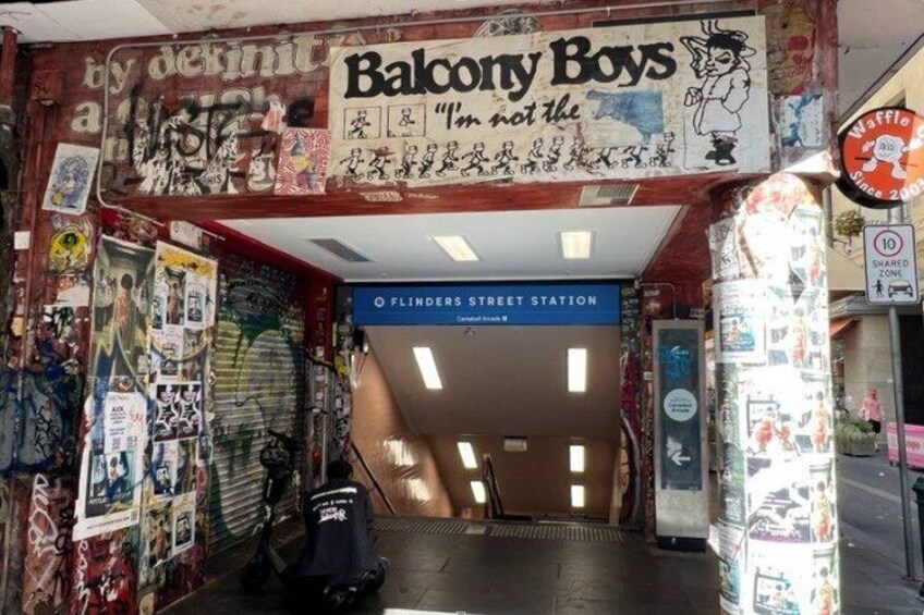 A subway entrance with graffiti and posters, a sign for 'Balcony Boys,' and a 'Flinders Street Station' sign. 4