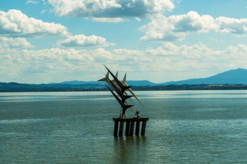 A sculpture on a pier in a body of water with mountains in the background. 2