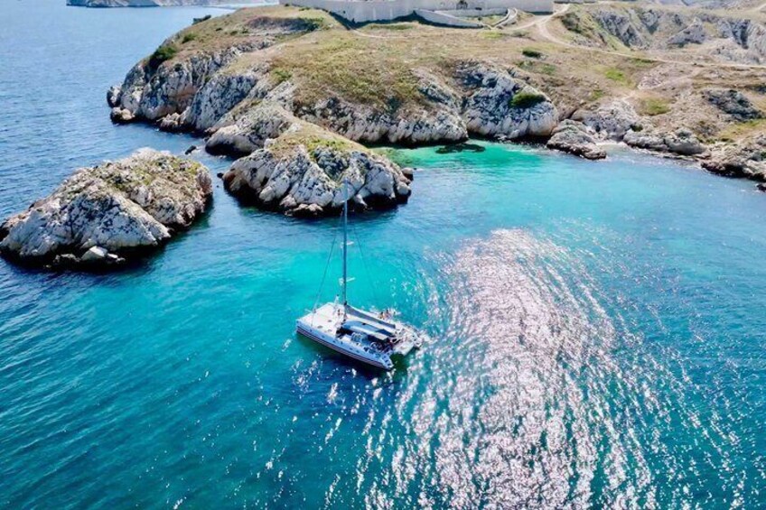 A sailboat anchored near rocky outcrops in clear turquoise waters. 1