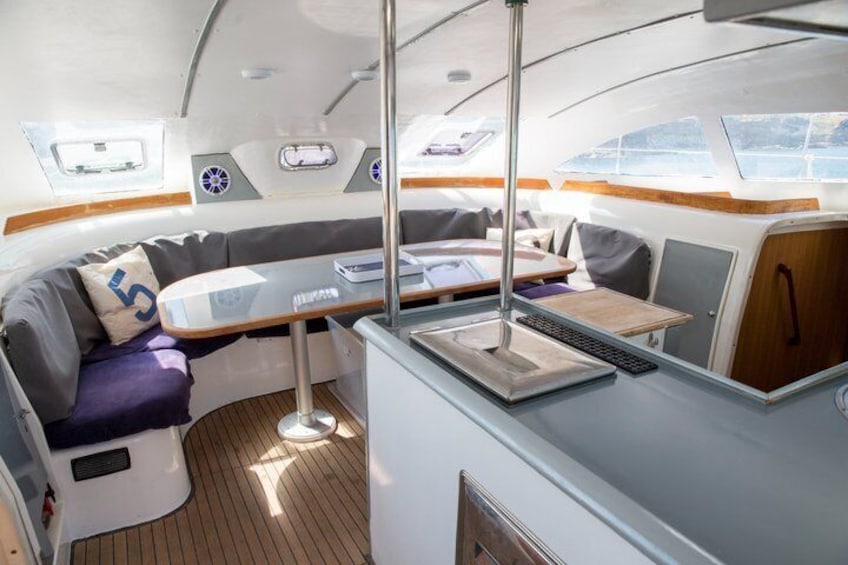 A boat's interior with a dining area, a cushioned seating area, and a control panel. 3