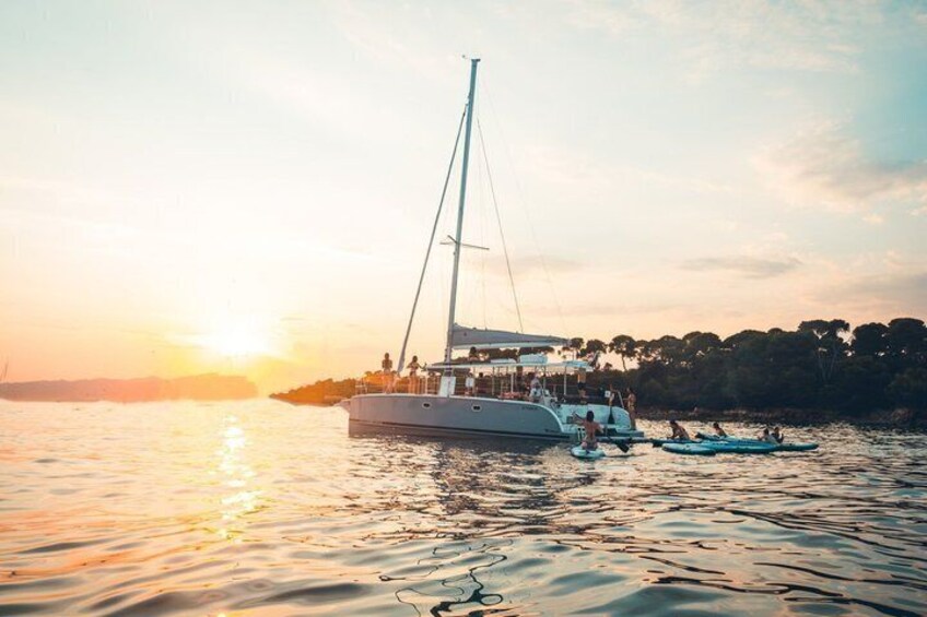 A sailboat with people on board, docked near a shoreline with trees. 4