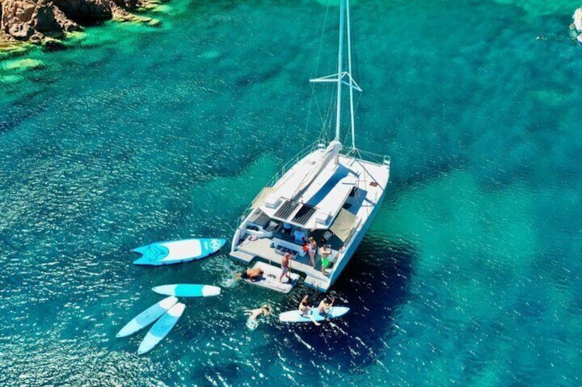 A sailboat with a cabin and multiple blue paddleboards floating in clear turquoise water. 1