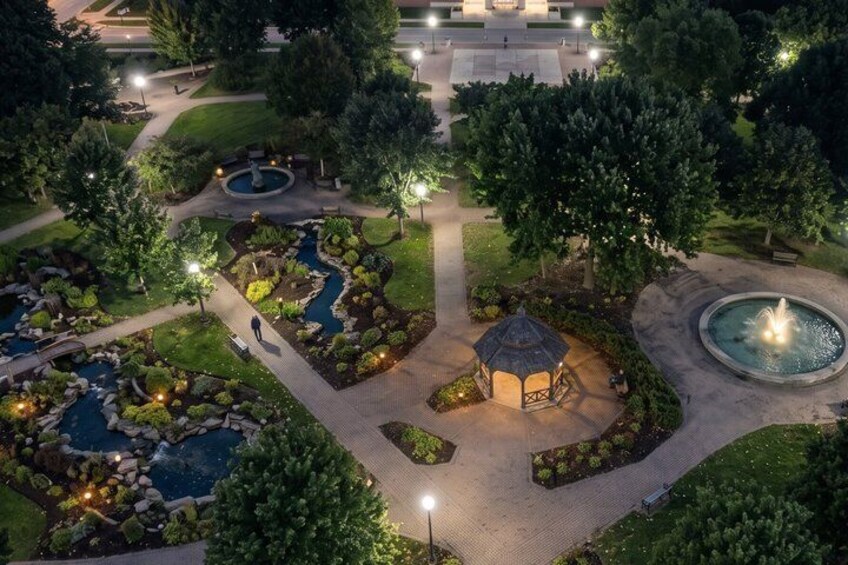 A well-lit park at night with a pond, gazebo, and walking paths. 3