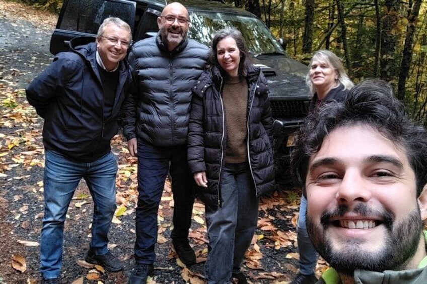 A group of people standing in a forested area with a vehicle in the background. 2