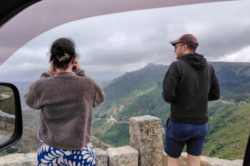Two people standing on a cliff overlooking a mountainous landscape. 1