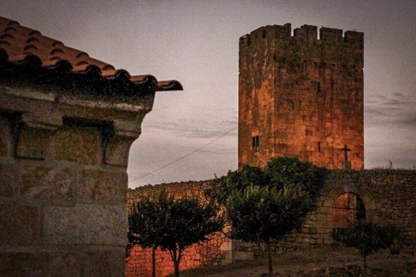 A stone tower with a cross on top, a stone wall, and a tree in front. 3