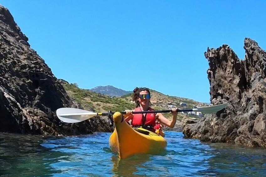 A person kayaking in clear water with rocky cliffs and hills in the background. 2