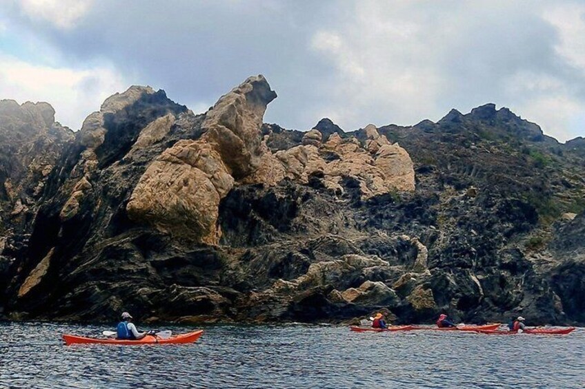 Kayakers in red canoes on a calm body of water with rocky cliffs in the background. 5