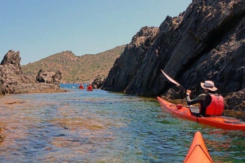 A kayaker in a red kayak on a calm river, surrounded by rocky cliffs and clear blue water. 3