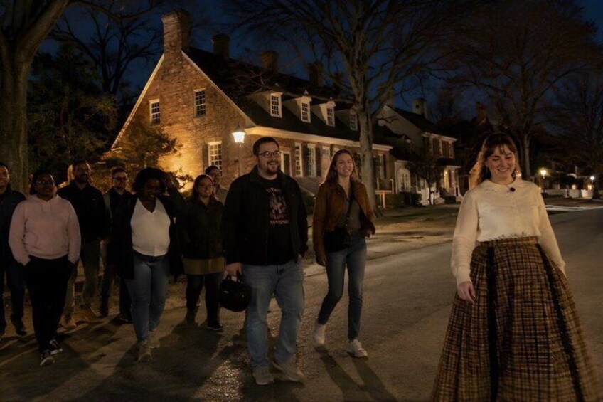 A group of people walking on a street at night, a house with lights on, and bare trees. 1