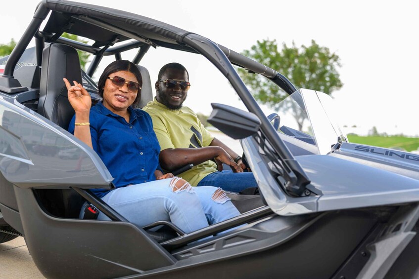 Two people in a convertible car with a visible logo on the side. 3