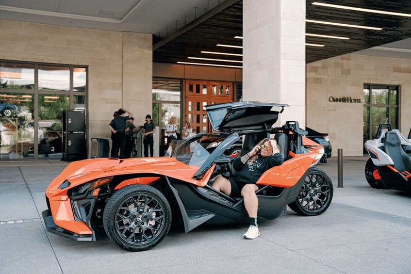A person sitting on a red sports car with its hood open, parked in front of a building with a sign that reads 'OMNI Hotel'. 5