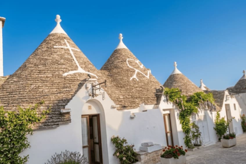 A row of traditional conical-roofed buildings with white walls and a clear blue sky. 2