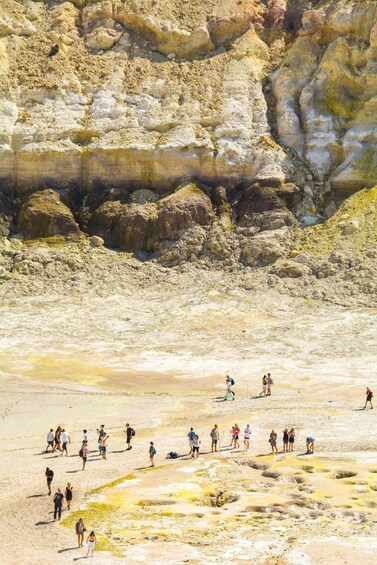 A group of people walking on a rocky terrain with yellowish mineral deposits. 1