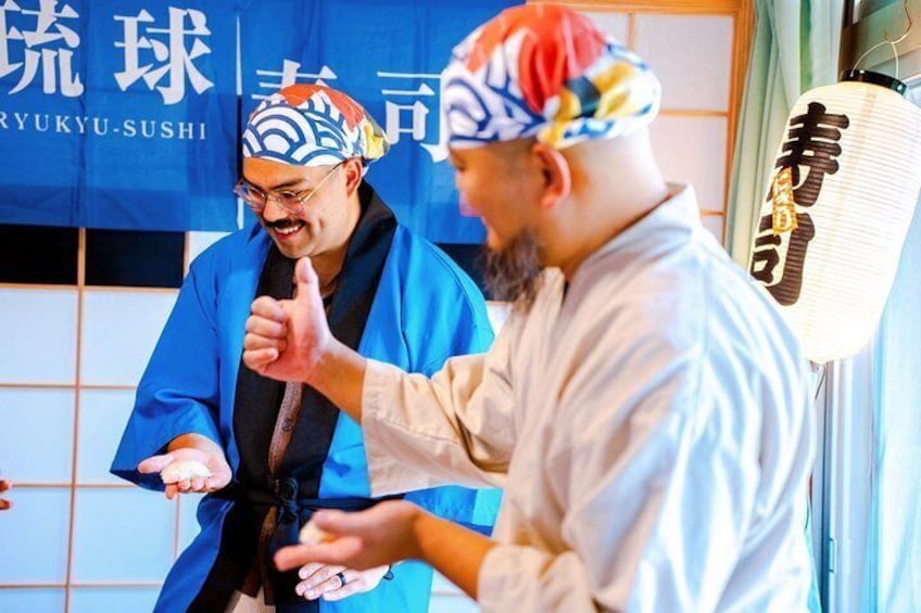 Two people in traditional Japanese attire, one giving a thumbs-up, with a blue banner in the background. 1