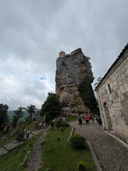 A rocky cliff with a small building on top, surrounded by greenery and a stone pathway. 5