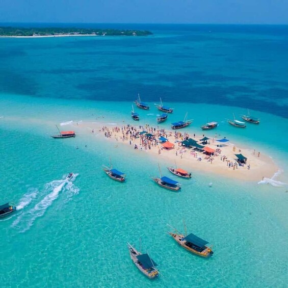A tropical beach with clear turquoise waters, a small island with people and colorful umbrellas, and several boats anchored nearby. 5