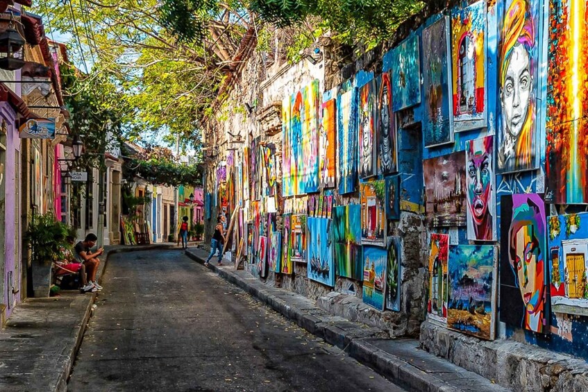 A street lined with colorful murals and graffiti, with buildings on either side and a few people walking. 5