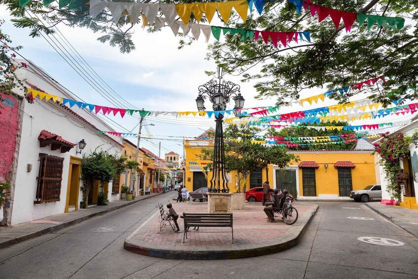 A street decorated with colorful triangular flags, a central lamp post, and a bench. 3