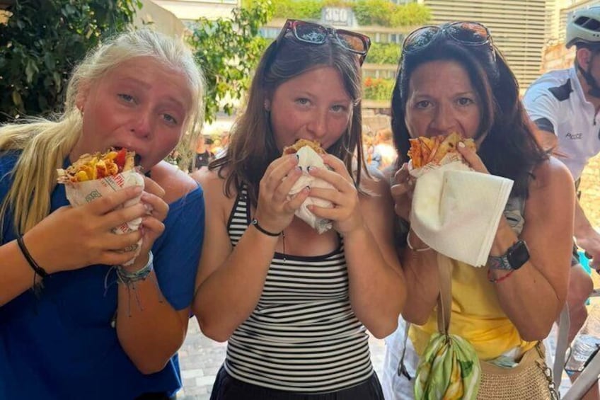 Three people eating food from paper containers outdoors. 1