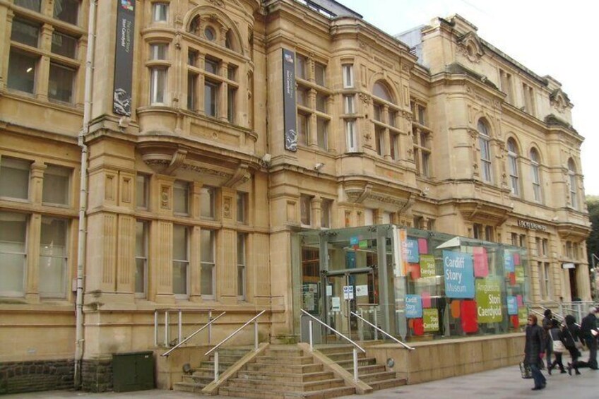 A historic building with ornate architecture, a glass entrance, and a sign for the Cardiff Story Museum. 4