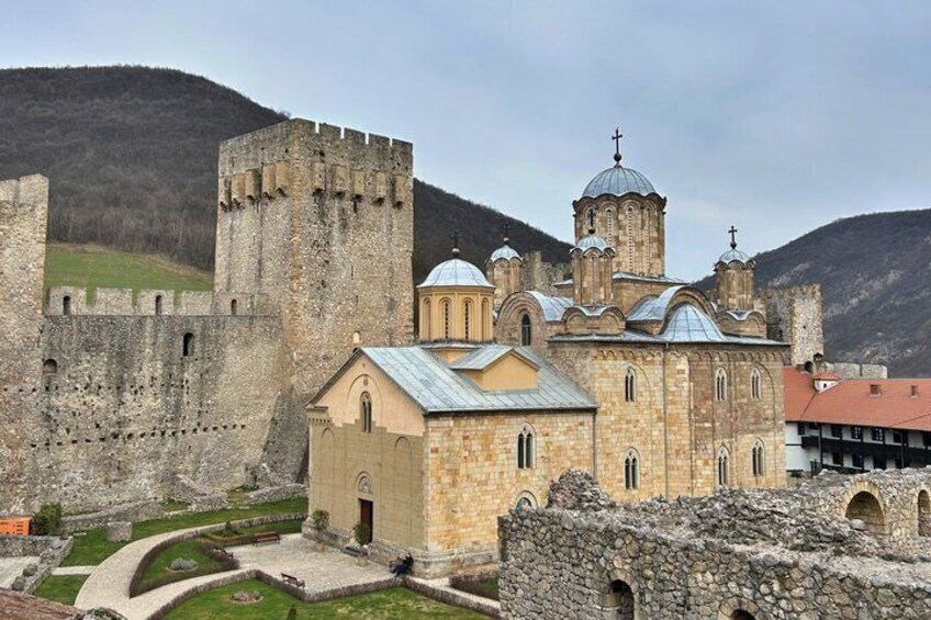 A historic stone church with a bell tower, surrounded by a fortified wall and set against a mountainous backdrop. 1