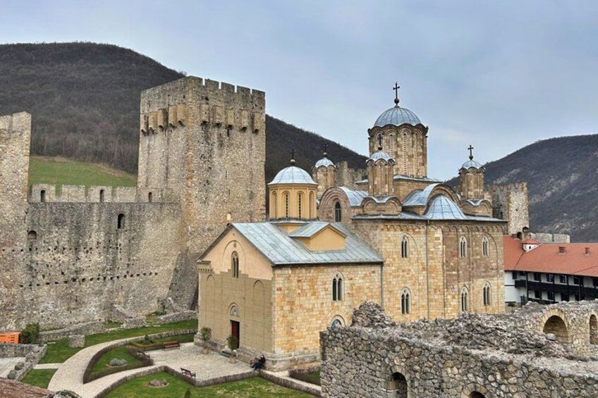 A historic stone church with a bell tower, surrounded by a fortified wall and set against a mountainous backdrop. 1