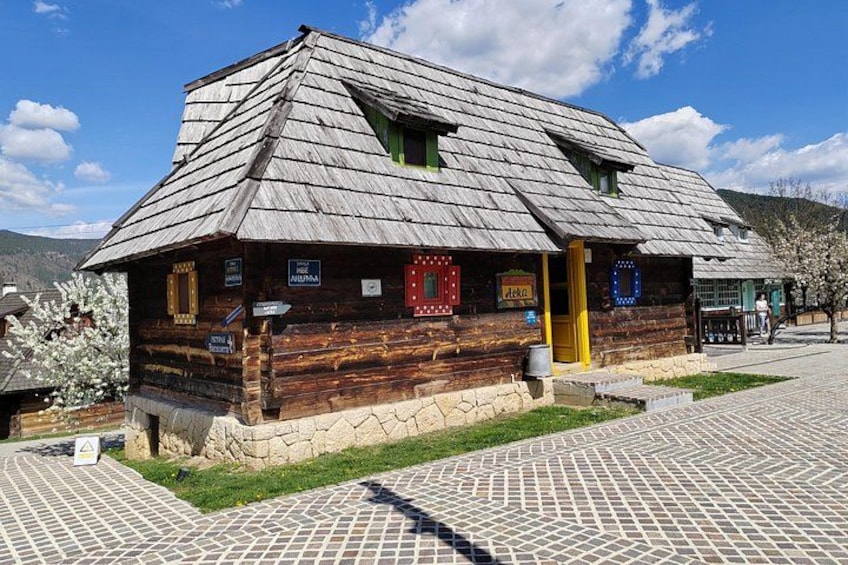 A wooden house with a sloped roof, a stone foundation, and a paved walkway. 2