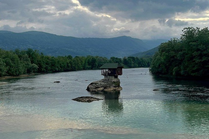 A river with a small house on a rock, surrounded by lush greenery and mountains in the background. 4