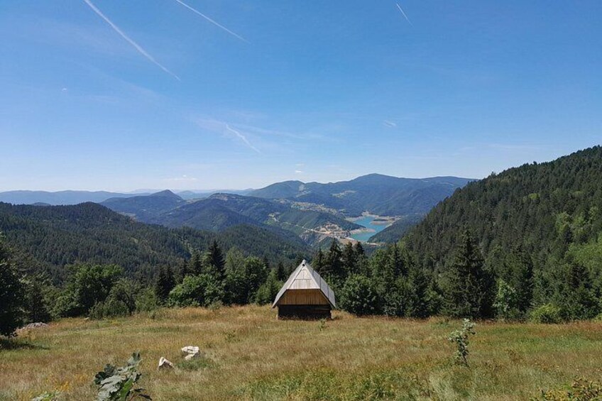 A wooden cabin in a forested valley with a lake in the distance. 5