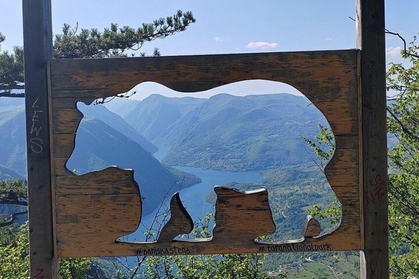 A wooden sign with a bear silhouette, surrounded by a mountainous landscape. 3