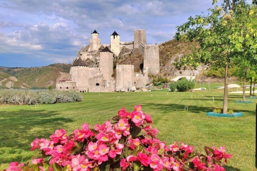 A castle with towers, surrounded by a well-maintained lawn and flowering plants. 1
