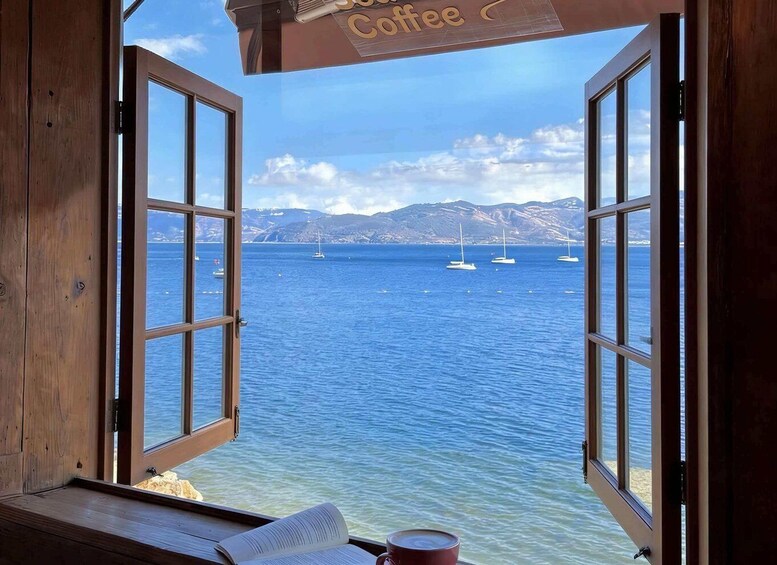 A wooden table with a book and a cup, an open window with a view of the sea and sailboats, and a sign reading 'Coffee'. 5