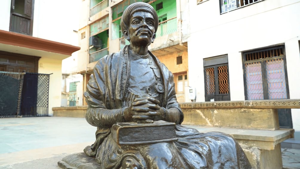 A statue of a seated figure holding a book, with a building in the background. 2