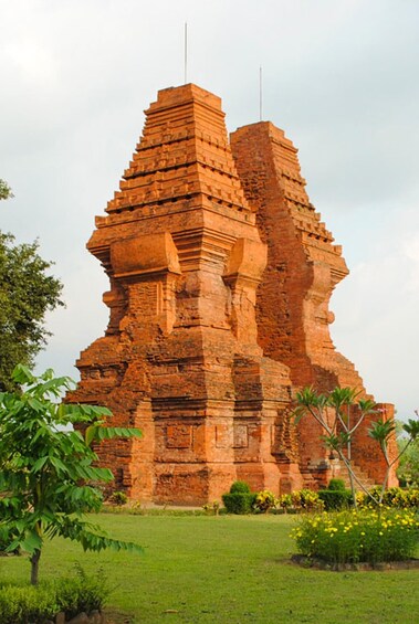 A large, ancient brick temple with a stepped pyramid structure, surrounded by lush greenery and flowering plants. 2